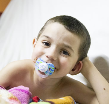 Foto de um menino segurando a cabeça deitado e sorrindo para a camera